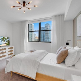 a bedroom with a bed tv dresser chandelier window and mirror